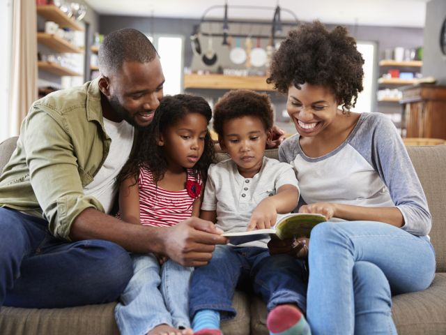 Family Sitting On Sofa In Lounge Reading Book Together